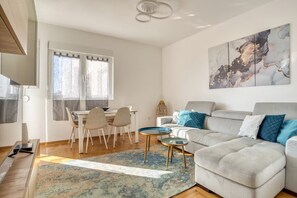 A modern living room with a sofa, a dining table with chairs, a coffee table, and a large abstract painting on the wall. - Baby Blue Apartment (Budva)