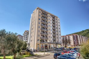 A multi-story residential building with balconies, a parking area with cars, and a clear sky. - Baby Blue Apartment (Budva)
