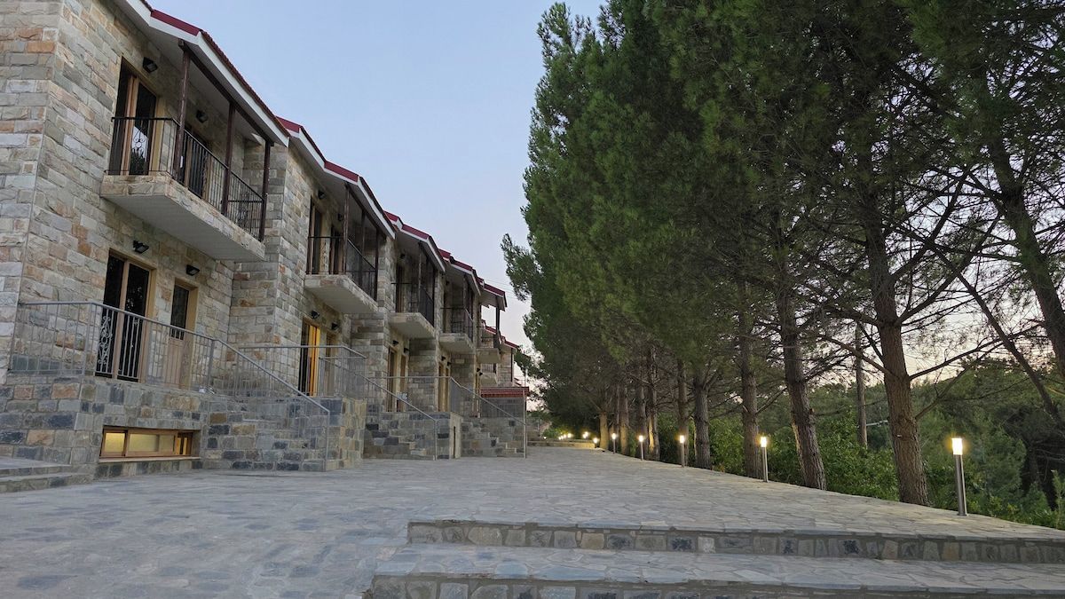 A stone building with multiple balconies, a staircase leading to the entrance, and a pathway lined with trees.