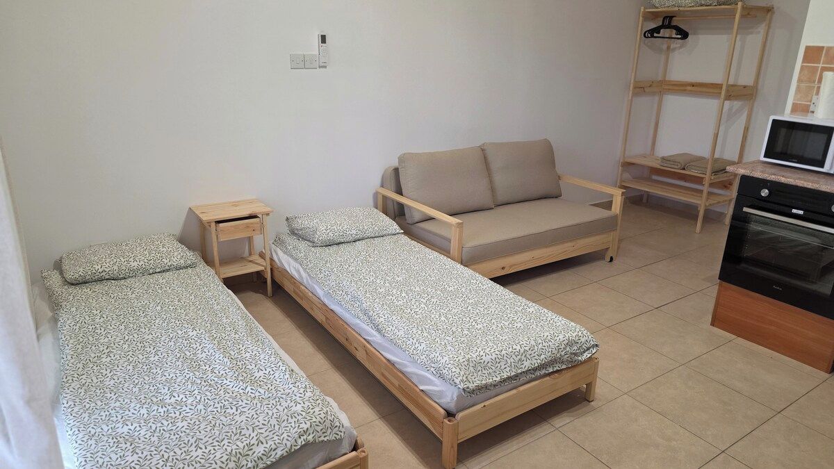 A compact room with three single beds, a sofa, a wooden shelf, and a microwave.