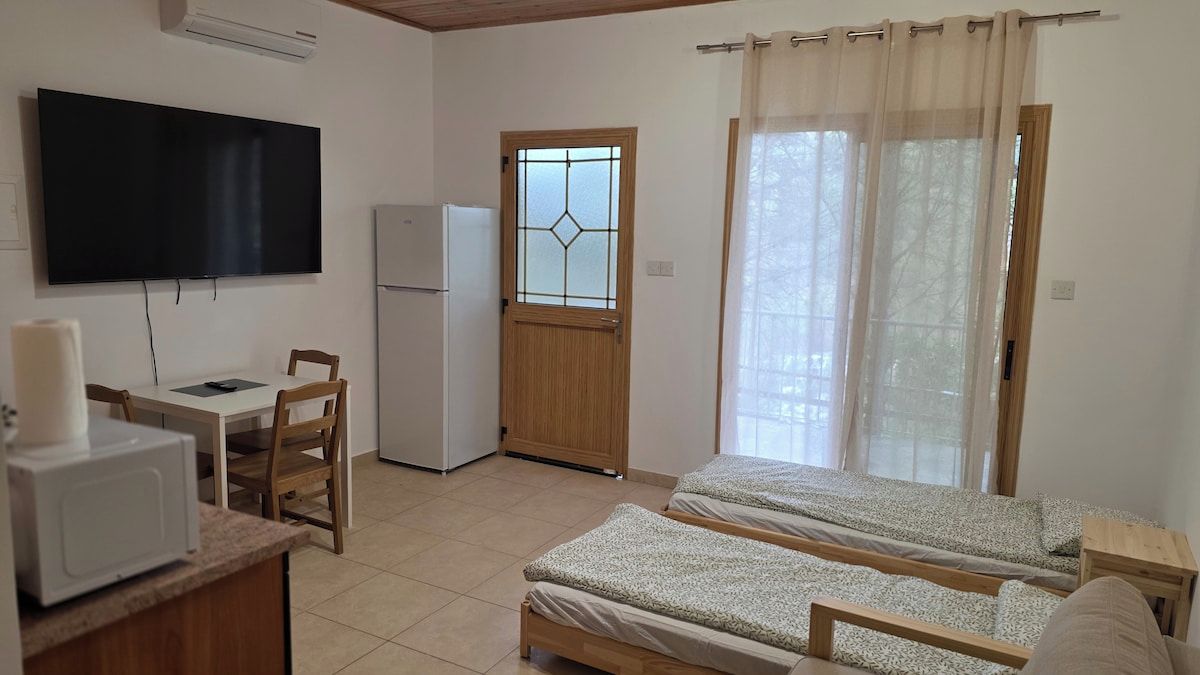 Una habitación con una cama, un escritorio, una silla, un televisor, un refrigerador y una ventana con cortinas.