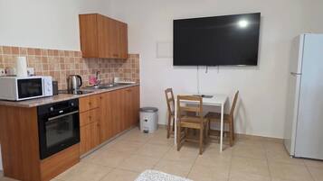 A compact kitchen with wooden cabinets, a microwave, a stove, a sink, and a television mounted on the wall.