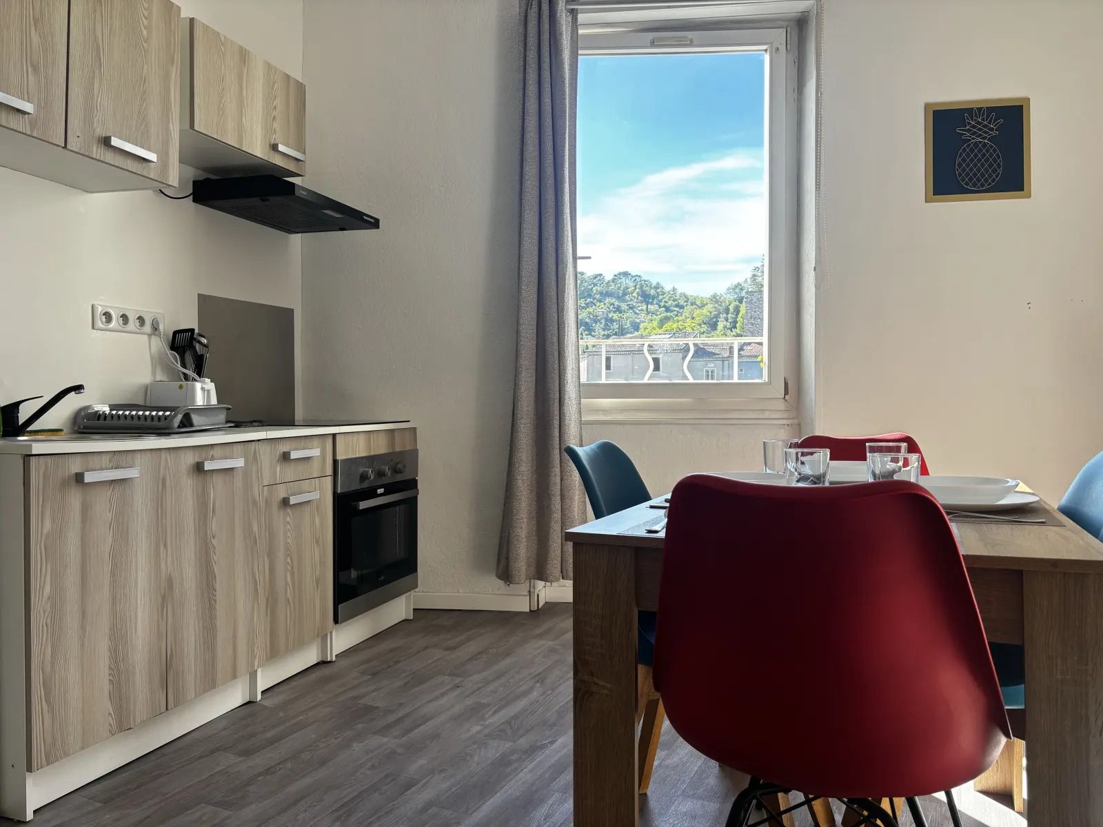 A modern kitchen with wooden cabinets, a built-in oven, and a window with a view of greenery.