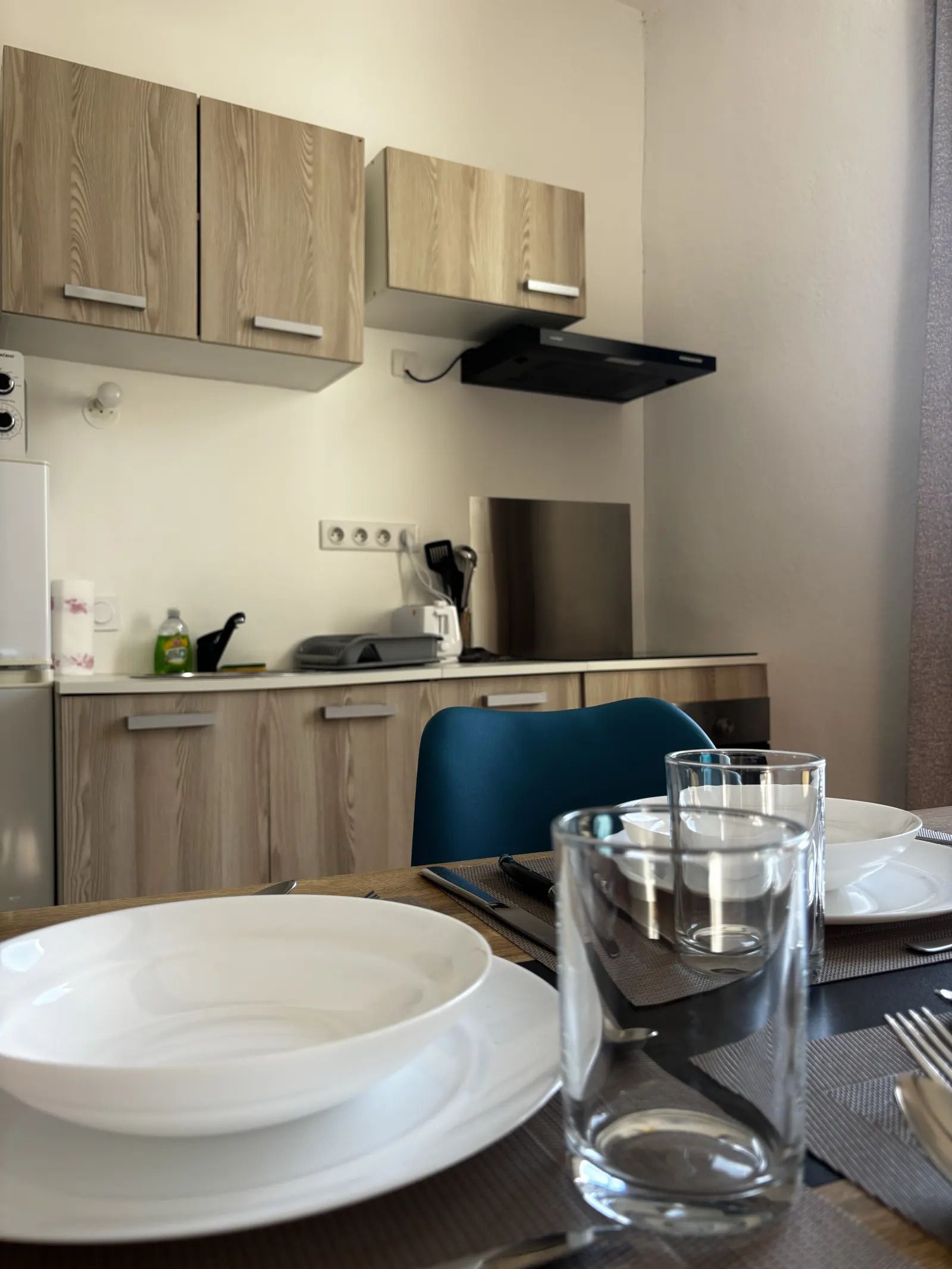 A modern kitchen with wooden cabinets, a black range hood, and a dining area with a table set for two.