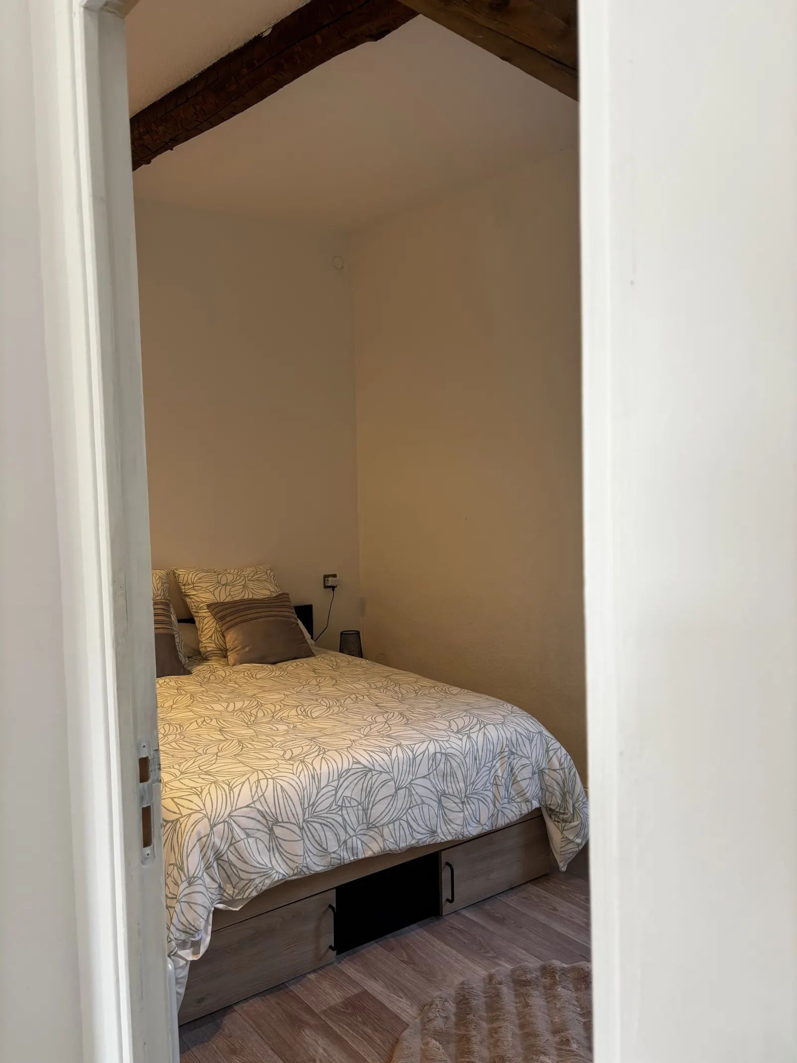 Een slaapkamer met een bed, een nachtkastje en een stopcontact op de muur.