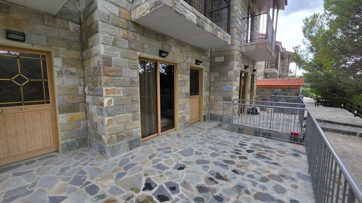 Un edificio de piedra con entrada empedrada, puerta de madera y un balcón con barandilla metálica.