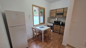Una cocina compacta con refrigerador, una mesa de comedor con sillas, armarios de madera y un ventanal.