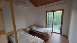 Una habitación con dos camas de madera, una mesita de noche, una ventana con vistas a zonas verdes y un equipo de aire acondicionado.