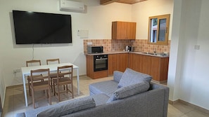 Un espacio habitable compacto con comedor, kitchenette y un sofá gris.