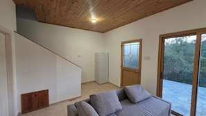 Una habitación con techo de madera, un sofá gris, un refrigerador pequeño y una ventana con vista a árboles.