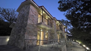 Un edificio de varios pisos de piedra con balcones, una escalera e iluminación exterior.