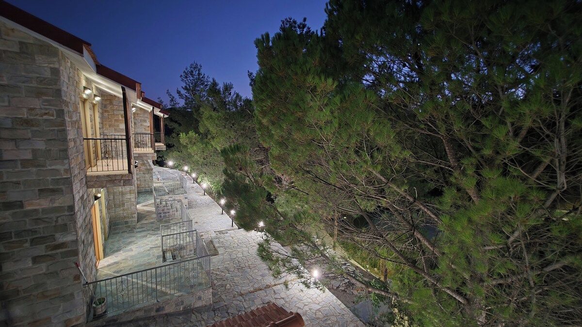 A stone building with a staircase leading to a balcony, surrounded by trees.