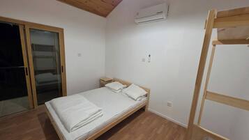A single bed with a wooden frame and white bedding in a room with a wooden floor and a ceiling with wooden beams.