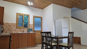Una cocina con armarios de madera, una mesa de comedor con sillas, un refrigerador y un ventanal con vista a árboles.