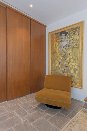 A room with a large wooden wardrobe, a sofa, and a large framed artwork on the wall.