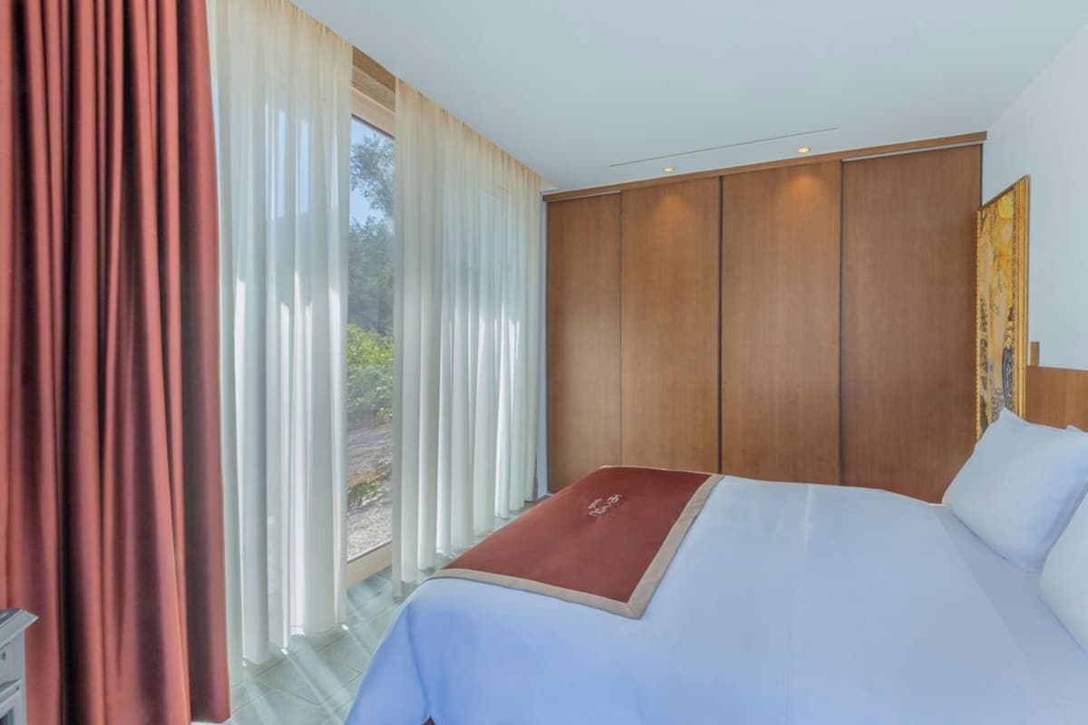 A hotel room with a large bed, a wooden headboard, and a view of greenery outside.