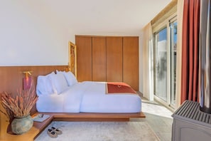 A modern hotel room with a large bed, a wooden wardrobe, a sliding glass door to the outside, and a small table with a vase and slippers.