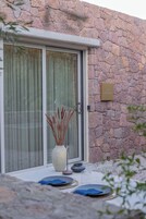 Un muro de piedra con un cristalero corredero, una planta en maceta y un cartel que indica una cabaña.