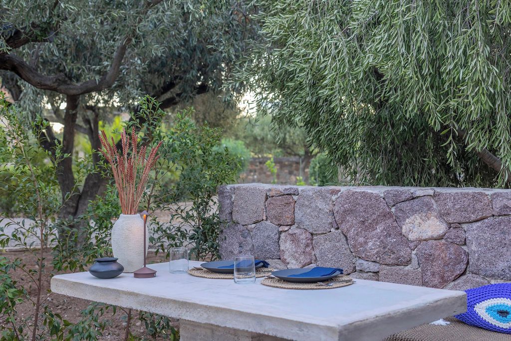 Un área de comedor al aire libre con una pared de piedra, una mesa dispuesta con platos, vasos y un florero con plantas secas.
