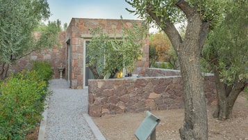 A stone building with a door and windows, surrounded by gravel paths and greenery.