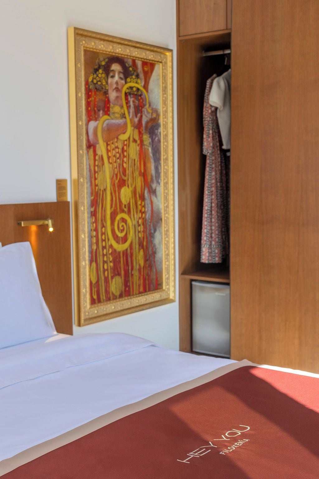 Habitación de hotel con una cama, un cuadro, un armario y un pequeño mueble.