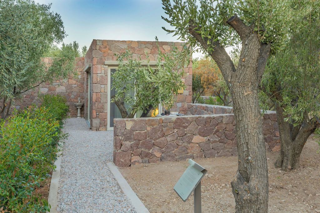 Un bâtiment en pierre doté d’une porte et de fenêtres, entouré de chemins de gravier et de verdure.