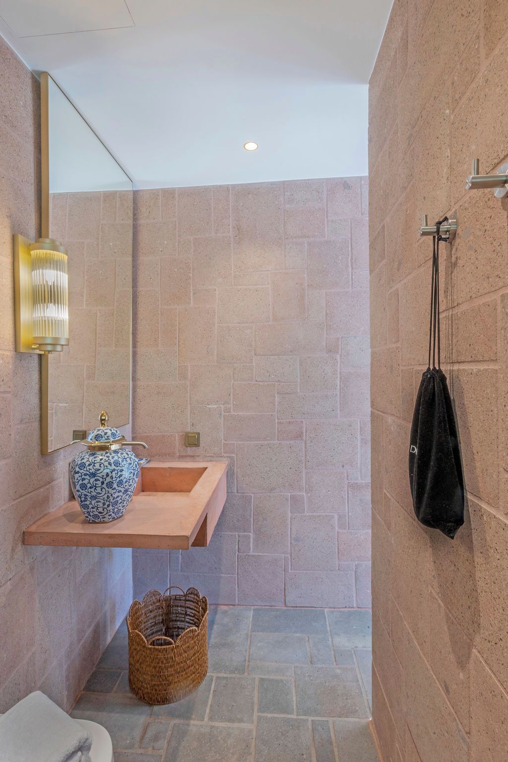 A bathroom with a stone wall, a wooden vanity, a blue vase, a wicker basket, and a towel rack.