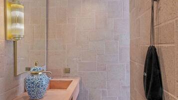 A bathroom with a stone wall, a wooden vanity, a blue vase, a wicker basket, and a towel rack.