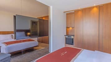 A hotel room with two beds, a flat-screen TV, a small kitchenette, and wooden paneling.