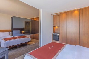 A hotel room with two beds, a flat-screen TV, a small kitchenette, and wooden paneling.