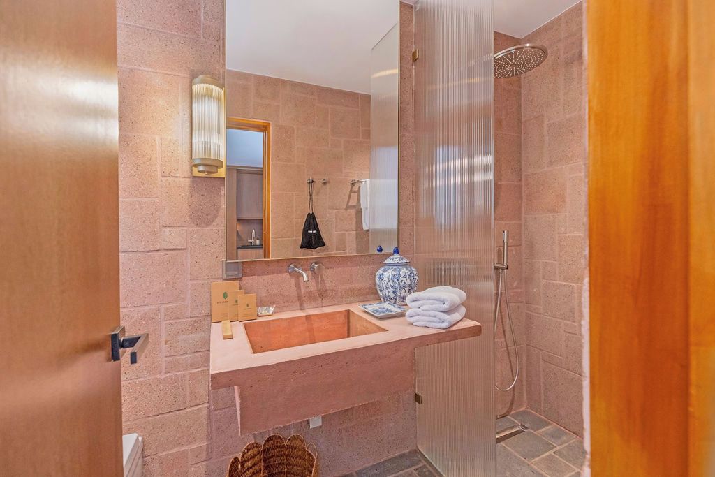Un baño con pared de piedra, un lavabo con un florero y una ducha.