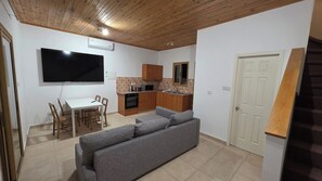 A compact living space with a dining area, kitchenette, and a gray sofa. - Platres Villas: House 1 - Apartment with Mountain View (Kato Platres)