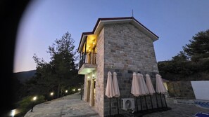 A stone building with a balcony, outdoor seating with umbrellas, and an air conditioning unit. - Platres Villas: House 1 - Apartment with Mountain View (Kato Platres)