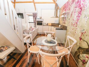 A cozy living area with a glass-top dining table surrounded by wicker chairs, a sofa, and a kitchen in the background. - The Apple Store at Gileston Manor (Barry)