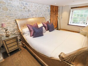 A bedroom with a stone wall, a wooden bed frame, and a window with a view. - The Apple Store at Gileston Manor (Barry)