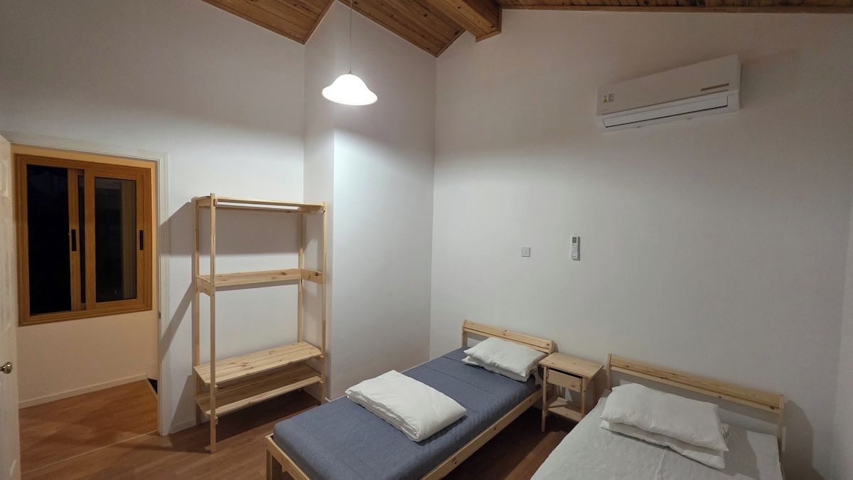 A room with two wooden beds, a bench, and a ceiling fan.