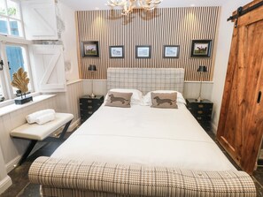 A bedroom with a large bed, a bench, a chest of drawers, a wardrobe, and a wall with framed pictures. - The Stalls at Gileston Manor (Barry)