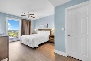 A bedroom with a bed, bedside lamps, a ceiling fan, a door, and a view of greenery outside. - Laketown Wharf 1731 (Panama City Beach)