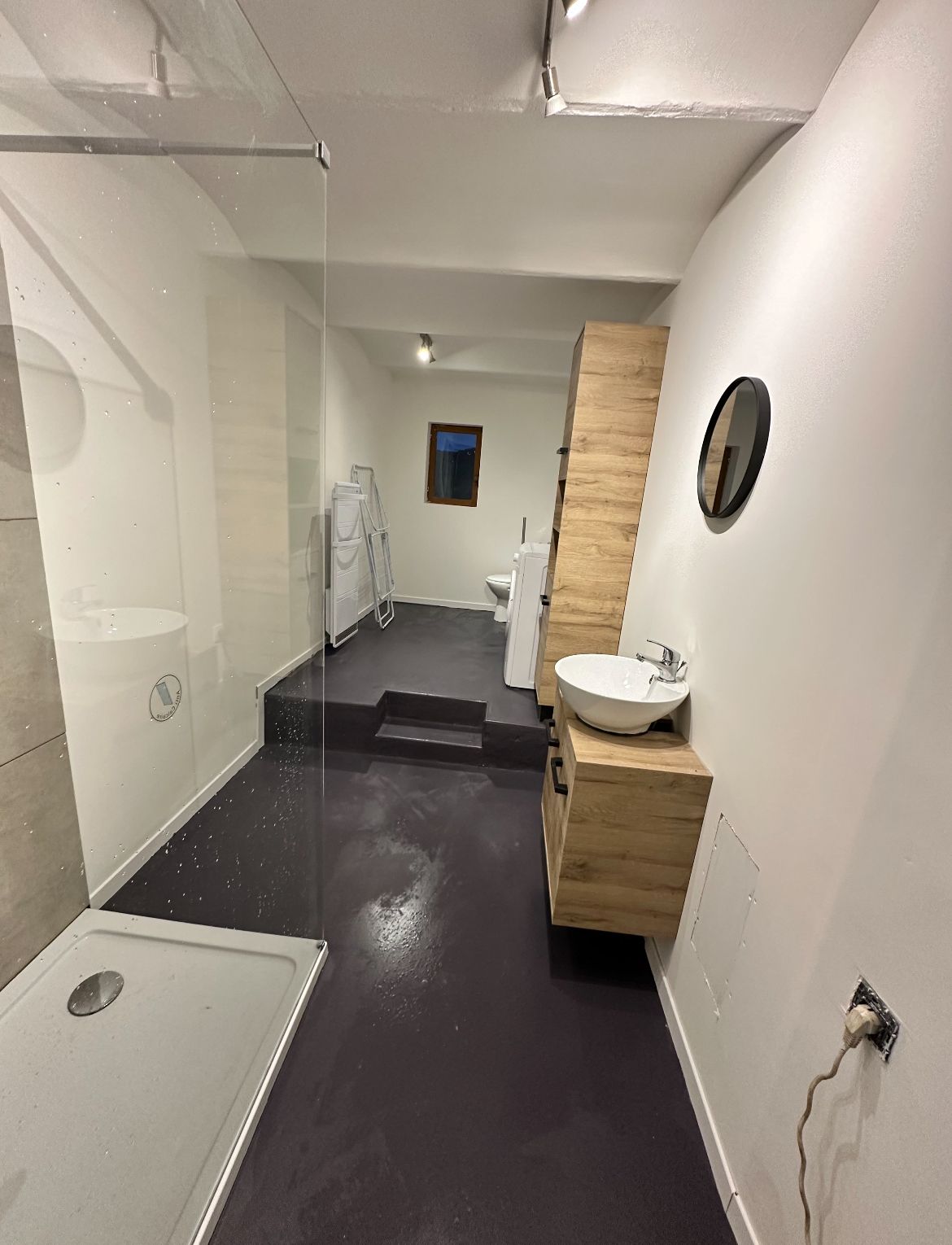 A modern bathroom with a glass shower enclosure, a white sink, and a wooden vanity.