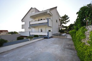 A modern two-story building with balconies, a paved courtyard, and a green hedge. - Spacious 110 m2 apartment with terrace and garden, just 30m from the beach (Podstrana - Mutogras)