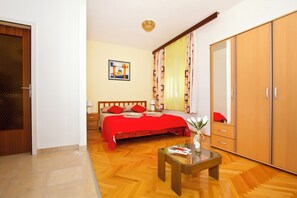 Une chambre à coucher avec un lit en bois, une couvre-lit rouge, une armoire en bois et une petite table sur laquelle est posé un vase.
