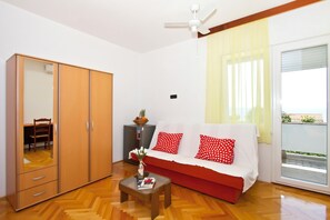 Ein Zimmer mit einem Holzschrank, einer Couch mit roten Kissen, einem kleinen Tisch mit einem Buch und einem Deckenventilator.