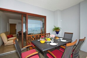 Un coin repas avec une table dressée pour quatre personnes, des chaises, une plante en pot et une vue à travers une porte vitrée.
