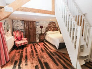 A bedroom with a stone wall, a wooden floor, a bed, a chair, and a staircase. - The Coach House at Gileston Manor (Barry)
