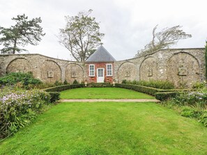 A traditional stone building with a red brick facade, a white door, and a small garden with a manicured lawn and hedges. - The Coach House at Gileston Manor (Barry)