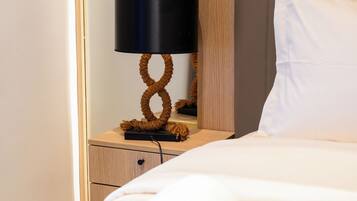 A neatly made bed with a rolled white towel, a bedside table with a lamp, and a wooden headboard.