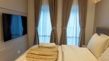 Habitación de hotel con cama, televisión montada en la pared y ventana con cortinas.