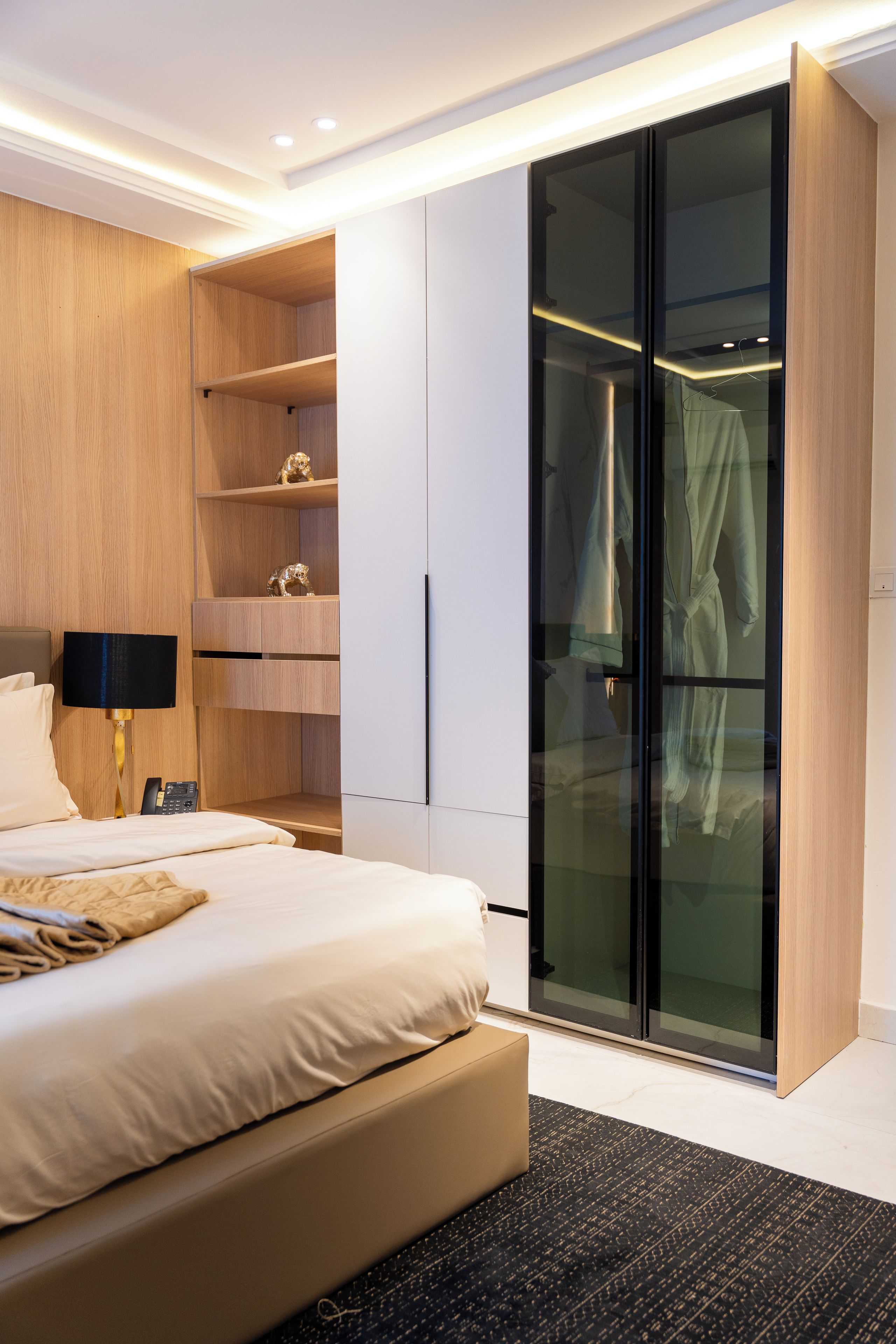 Un dormitorio moderno con cama, mesita de noche, lámpara, armario y armario de cristal.
