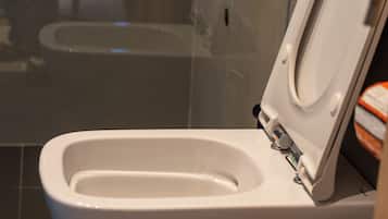 A modern toilet with a closed lid, a visible flush handle, and a wall-mounted bidet attachment.
