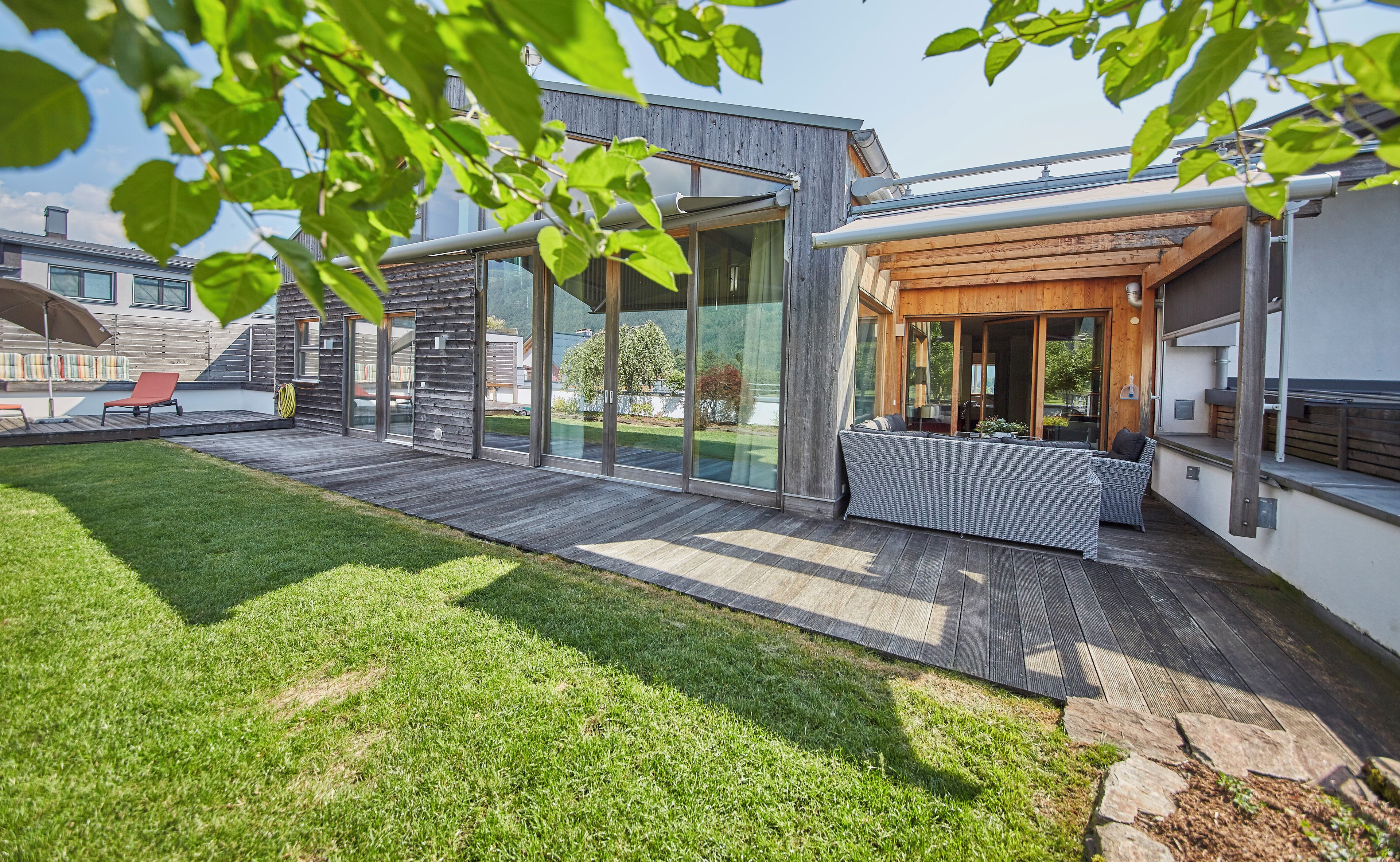 Een modern huis met een terras, een patio met buitenmeubilair en uitzicht op een meer.